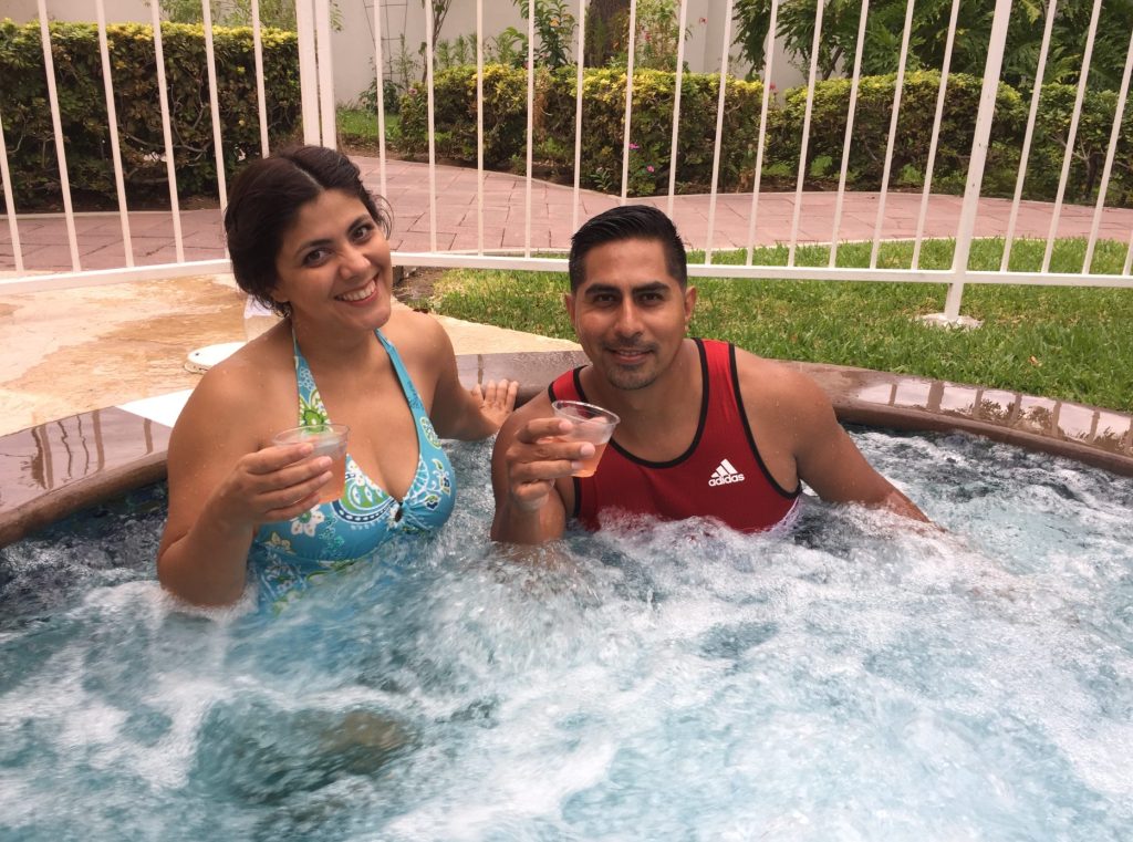 Two smiling people in a hot tub with drinks in their hands