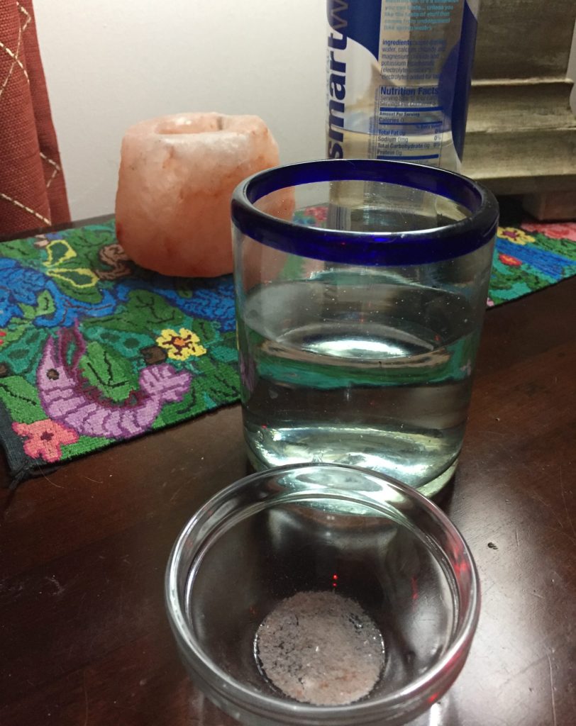 A glass of water and a small glass bowl with some pink Himalayan salt