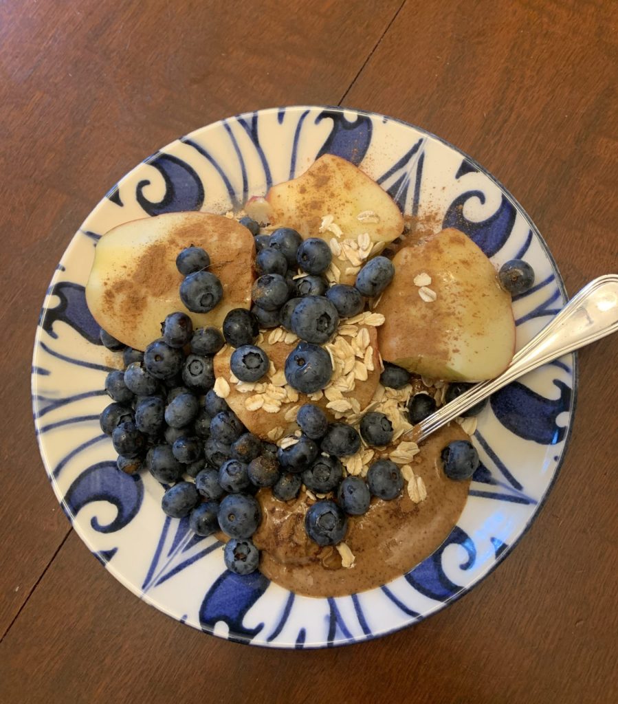 A plate of cut apple with cinnamon, almond butter, blueberries and oats
