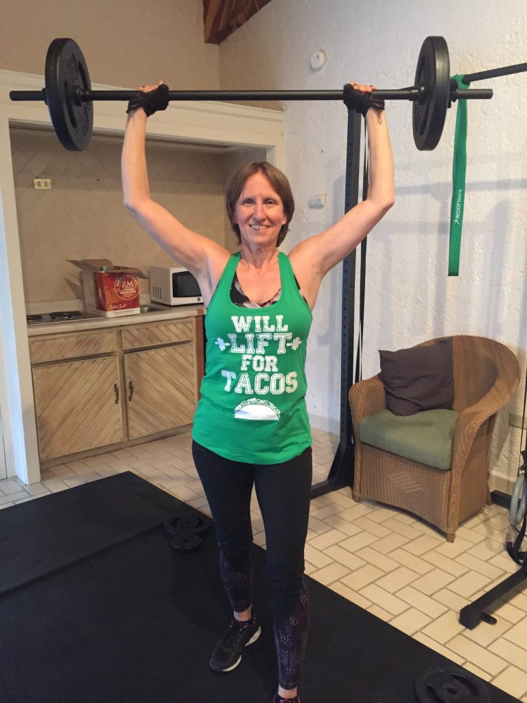 The author holding a barbell overhead and wearing a shirt that says Will Lift for Tacos