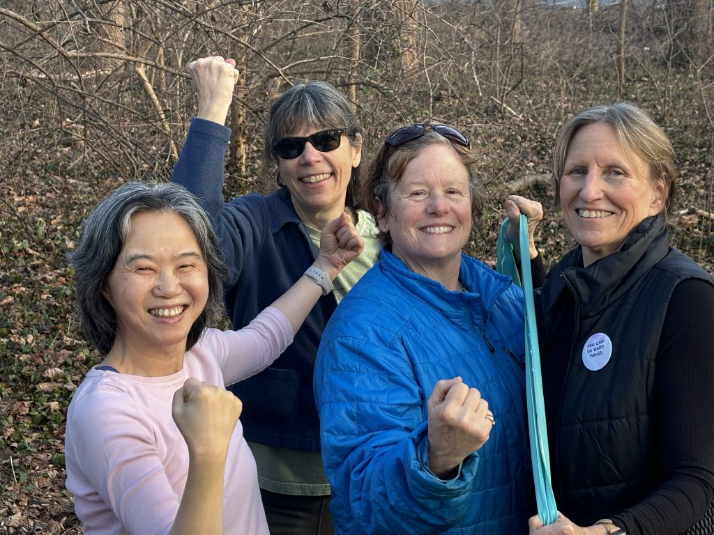 Four women outdoors looking strong, raising fists or holding a resistance band