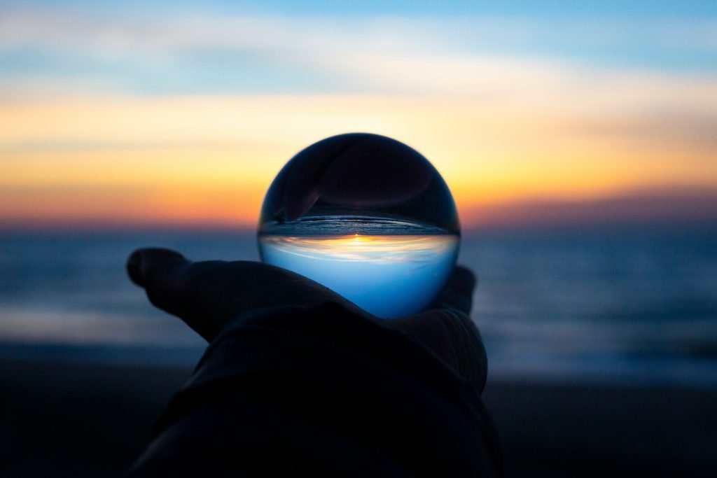 Glass sphere being held up on hands with a sunset in the background